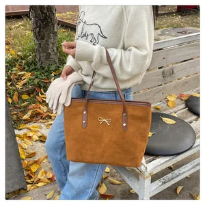 Close-up of brown suede tote bag with elegant golden metal bow and slim shoulder straps