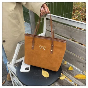 Close-up of brown suede tote bag with a small gold bow detail and dark leather handle