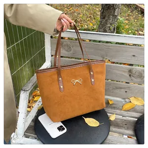 Close-up of brown suede tote bag featuring a golden bow metal accessory and leather strap