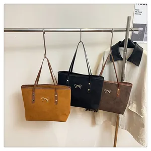 Detailed close-up of suede tote bags with golden bow metal accents in mustard and coffee