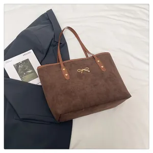 Detail of suede texture tote bag with golden bow hardware and contrast handle