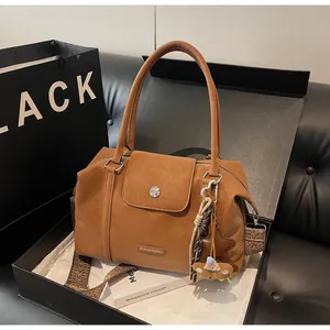 Close-up of caramel faux leather bag with wide jacquard strap and bear charm in a gift box