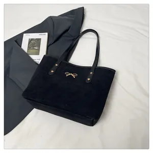 Detail of black suede tote bag featuring a decorative gold bow and reinforced rivets