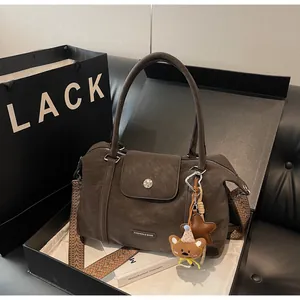 Detail of coffee brown PU leather bag with wide woven strap and bear charm in a gift box