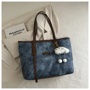 Detail of blue textured tote bag with brown leather handles and a white cloud plush charm