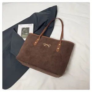 Detail of dark brown suede tote bag with golden bow hardware and rivet accents