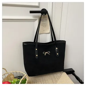 Close-up of minimalist black tote bag featuring a decorative gold metal bow detail