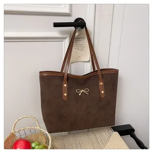 Detailed macro view of dark brown suede tote bag featuring golden bow and rivet accents