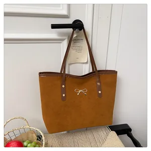 Detail view of brown suede tote bag with gold bow ornament and long shoulder strap