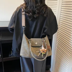 Grey hobo pillow bag with patterned wide strap and bear pendant in cozy interior