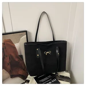 Detailed macro view of black suede tote bag with elegant golden bow metal hardware