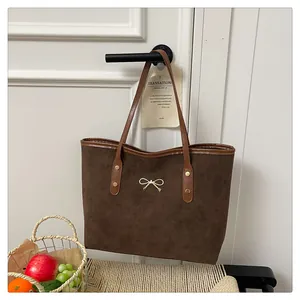 Detail of a large brown suede tote bag with a golden bow charm on a white door