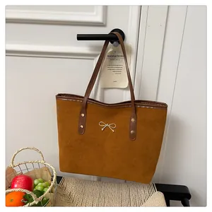 Close-up of a caramel suede tote bag featuring a small gold metal bow and brown leather straps