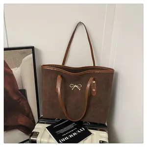 Detail of dark brown tote bag showing suede texture and golden bow hardware on a suitcase