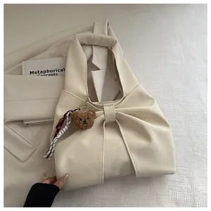 Detail of cream handbag featuring bow-tie pleats, plush bear charm and striped ribbon