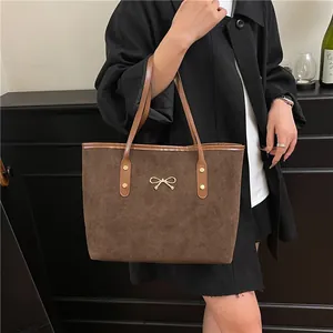 Brown suede tote bag with golden bow and rivets shown in a stylish commuter look