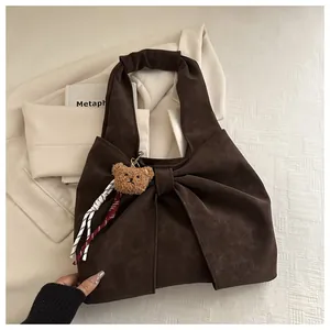 Detail of a dark brown suede handbag featuring a large bow and a cute teddy bear charm