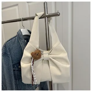 Close-up of cream bow-shaped handbag with plush bear charm and wide shoulder strap