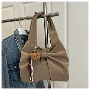 Detail of khaki tote bag with large decorative bow and cute brown teddy bear keychain