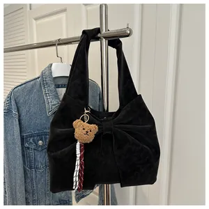 Detail of black bow shoulder bag with teddy bear pendant on a metal rack