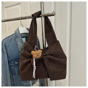 Close-up of brown bow-shaped tote bag with plush bear charm and striped ribbon detail
