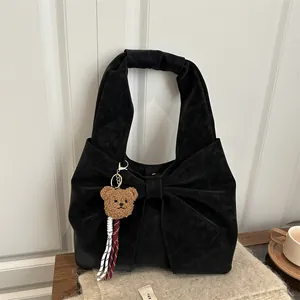 Retro black bow knot handbag with plush bear charm on soft beige fabric background