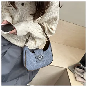 Detail of blue denim hobo bag with brown leather trim and silver M logo buckle