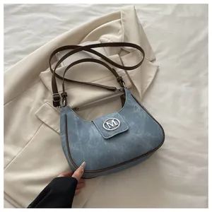 Detail of blue denim crescent bag with silver M logo buckle on a beige blazer