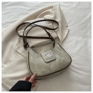 Detail of green textured faux leather bag featuring a silver metal M logo and brown trim