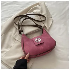Close-up of pink crescent shoulder bag with suede texture and metallic M logo detail