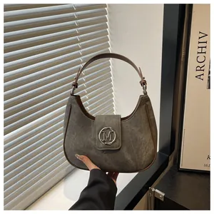 Detail of taupe suede crescent hobo bag with metallic M logo and adjustable handle
