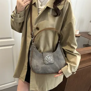 Chic grey crescent moon handbag with brown leather trim and metallic M logo on beige coat