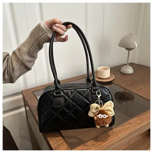 Detail of black quilted bowling bag with plush monster charm on wooden table