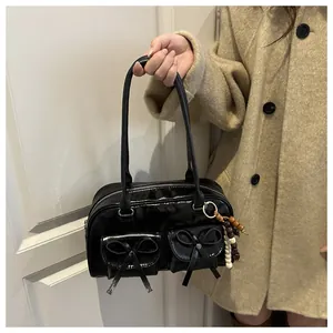Detail of black glossy leather bag featuring bow pockets and a beaded charm accent