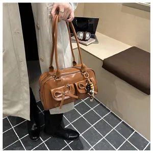 Detailed close-up of a brown leather bowling bag with bow accents and beaded charm strap