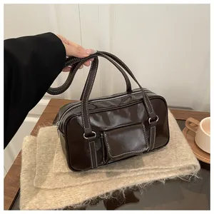 Detail of dark brown glossy handbag featuring white contrast stitching and silver hardware