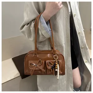 Caramel retro bowling bag with bow pockets and beaded charm shown on model's shoulder