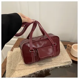 Detailed top view of a glossy burgundy red shoulder bag on a beige knit fabric