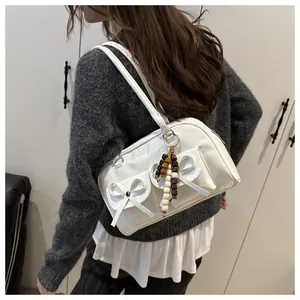 Detail of white leather shoulder bag with decorative bows and colorful beaded charm