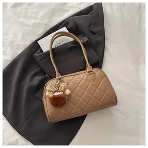 Detailed view of brown quilted bowling bag with a cute plush charm on a grey blazer