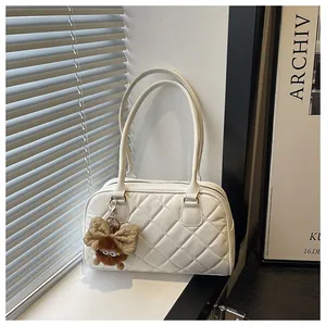 Detail of white quilted bowling bag with slim shoulder straps and brown plush bow charm