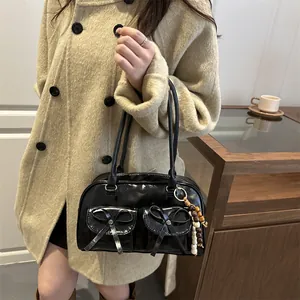 Glossy black bowling bag with bow detail and wooden bead charm on a beige coat