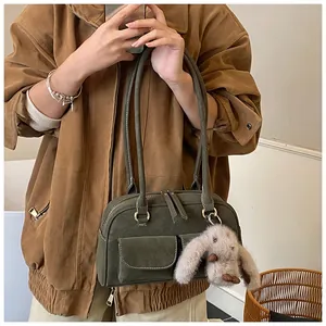 Detail of dark green suede shoulder bag featuring beige stitching and plush rabbit charm