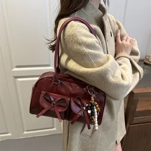 Glossy deep red bowling bag with bow details and bead charm worn by a model