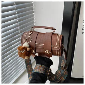 Brown retro handbag detail featuring gold rivets, plush monster charm, and patterned strap