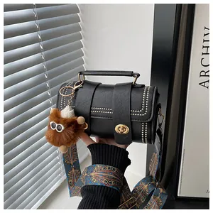 Detail of black leather barrel bag with gold studs, ethnic strap and plush charm