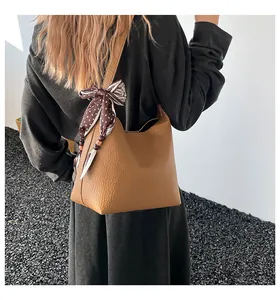 Detail of brown textured leather crossbody bag featuring a stylish polka dot silk scarf