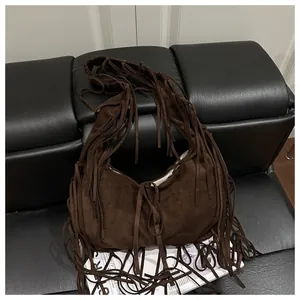 Détail d'un sac demi-lune en daim marron foncé avec de longues franges sur un canapé noir