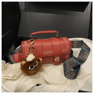 Detail of red cylindrical handbag with gold rivets, jacquard strap and plush charm