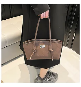 Detail of a brown quilted tote bag with silver logo plaque and decorative knots
